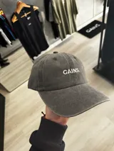 Gorra con visera de efecto acid wash en color gris oscuro, con diseño de seis paneles y el texto 'GAINS.' bordado en blanco en el frente.