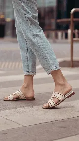 Sandalias planas de cuero negro, con diseño de tiras anchas interconectadas y punta cuadrada, decoradas con tachas metálicas doradas.