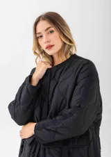 Chaqueta acolchada de color negro con diseño de costuras onduladas. Presenta cuello redondo, cierre frontal con botones a presión y dos bolsillos frontales tipo cargo con solapa y detalle de hebilla. Posee un corte holgado y mangas largas.
