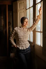 Blusa de muselina de algodón color beige, con diseño totalmente fruncido, cuello alto, mangas largas y terminaciones con volados en cuello, puños y ruedo.