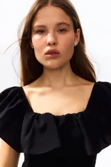 Vestido corto negro en tejido fruncido, de ajuste entallado con hombros descubiertos, escote cuadrado elástico y volado ancho con volumen en escote y bajo.