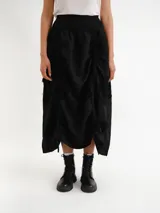 Pollera midi de diseño desestructurado en color negro, con cintura elastizada y detalles fruncidos con cordones ajustables a los lados.