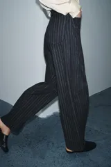 Pantalón de tiro medio con diseño balloon, confeccionado en tejido con patrón de rayas verticales. Presenta cintura con trabillas, cierre frontal con cremallera y botón, y cinco bolsillos.