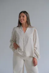 Blusa de color beige con cuello mao, cierre frontal con botones y mangas largas abullonadas. Presenta delicados bordados florales en la parte superior delantera.