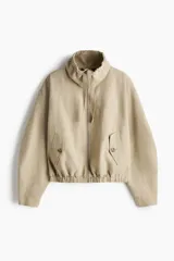 Campera beige en mezcla de lino, con cuello elevado con cordón ajustable, cierre frontal y bolsillos laterales con solapa y botón. Presenta hombros caídos y elástico revestido en el bajo.