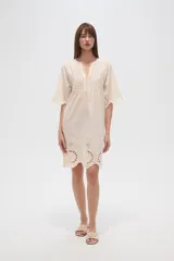 Vestido corto color crema, con escote en V y mangas 3/4. Presenta detalles de bordado inglés (broderie) en el canesú superior y en el ruedo inferior.