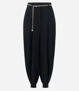 Pantalón de sastrería modelo aladim, color negro, confeccionado en crepé. Presenta pliegues en la cintura, corte holgado con piernas anchas que se estrechan en los tobillos y detalle de cinturón de cadena metálica.