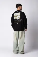 Buzo de cuello redondo y corte oversize, confeccionado en frisa suave. Presenta un diseño minimalista en color negro con un pequeño logo ovalado en el centro del pecho y una estampa sutil en el lateral inferior derecho.