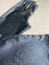 Pantalon oxford de cuerina sintetica en color negro, con textura y patron de imitacion cocodrilo y cintura elastizada.