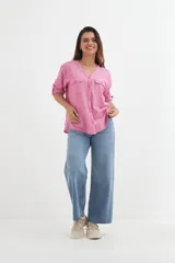 Camisa color blanco roto, de manga corta enrollada a 3/4, con escote en V y cierre frontal de botones. Presenta dos bolsillos de parche con solapa en el pecho.