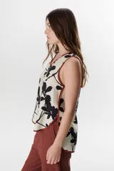 Top sin mangas de color blanco con escote en V y diseño holgado. Presenta un estampado artístico frontal en tonos azul y rojo, con terminaciones de vivo a contratono en color marrón.