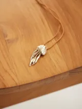 Collar con dije metálico en forma de medusa con acabado texturizado, montado sobre un cordón fino de color tostado.