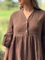 Vestido corto de lino color beige claro, con cuello mao, escote con botones de nácar, mangas tres cuartos con volados y ruedo con volado.