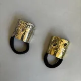 Accesorio para el cabello con banda elástica negra y aplique metálico dorado y plateado con textura irregular.