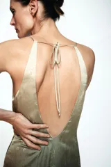 Vestido midi de estilo lencero con escote en pico y tirantes finos. Presenta un diseño degradado que va de un tono beige claro a un verde oscuro, con estampado floral sutil. Incluye lazada en la espalda y abertura en el bajo.