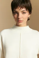 Polera de tejido de punto color blanco, con cuello alto acanalado, hombros caídos y detalle de costura vertical en el frente.
