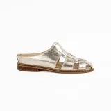 Zueco de cuero metalizado dorado, diseño artesanal con capellada en tiritas cruzadas estilo romano y talón descubierto con suela plana y pequeño taco de madera.