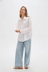 Camisa de algodón blanca, de corte oversize, manga larga y cuello camisero, decorada con apliques de strass y bordados sutiles en la parte delantera.