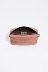 Bolso bandolera de tamaño mini confeccionado en nylon color rosado. Presenta una estructura blanda con cierre de cremallera superior, un bolsillo frontal con cierre y el logo metálico de Bimba y Lola en el frente. Incluye un asa de tejido regulable y extraíble mediante mosquetones plateados.