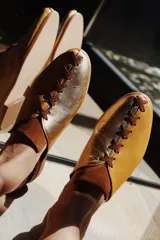 Zapatos tipo mules de punta cerrada y talón abierto, con diseño bicolor que combina cuero metalizado dorado y tono mostaza. Presentan detalles de costuras cruzadas en contraste sobre el empeine y suela baja.