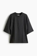Top de punto fino color gris oscuro, con cuello redondo, costuras decorativas frontales, hombros caídos y mangas al codo. Presenta un corte holgado con bajo levemente acampanado.