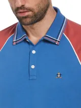 Chomba de hombre con mangas cortas raglán, color azul con mangas color ladrillo y detalles en blanco. Confeccionada en tejido interlock de algodón orgánico y logo bordado en el pecho.