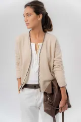 Saco básico de punto color marfil, confeccionado en lambswool, con corte entallado tipo chaquetita. Destaca por detalles de blonda tejida en los puños y a lo largo de la abertura frontal, con bordes en color contrastante.