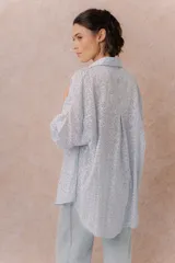 Camisa lila oversize de algodón con bordado floral calado tipo broderie, cuello camisero, manga larga y abotonadura frontal.