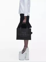 Cartera tipo tote de Marc Jacobs, confeccionada en cuero granulado color beige. Presenta el logo 'THE TOTE BAG' estampado en el frente, doble asa superior y correa de hombro ajustable y extraíble.