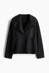 Chaqueta negra de corte relajado confeccionada en mezcla de algodón y lyocell, con solapas anchas redondeadas, hombros caídos, botonadura frontal y bolsillos delanteros de parche.