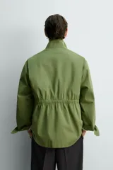 Parka estilo militar color verde, de corte relaxed fit, cuello subido y manga larga. Cuenta con bolsillos de plastrón con solapa en el pecho y en la cadera, cintura ajustable con cordón interior y cierre frontal con cremallera oculta por solapa con botones a presión.