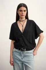 Blusa cruzada de manga corta, color negro, con escote en V profundo y detalle de botones o apliques plateados a lo largo del cruce frontal.