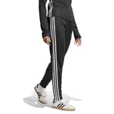 Pantalón deportivo Adidas Tiro 25 Essentials de corte ajustado, color negro con las icónicas tres tiras blancas laterales. Cuenta con cintura elástica con cordón de ajuste, bolsillos laterales con cierre y logo de la marca bordado en el frente.