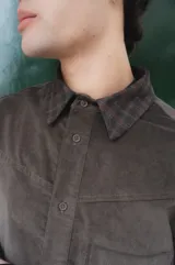 Camisa de corte boxy con estampado de cuadros pequeños en tonos oscuros. Presenta cuello camisero en color negro, cierre frontal con botones, canesú en la parte superior y un bolsillo en el pecho con etiqueta de la marca Kapsul Studio.