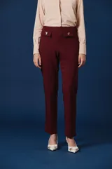 Pantalón de vestir color bordó, de corte recto y tiro alto. Presenta dos bolsillos frontales decorativos con solapas y detalles de broches metálicos en forma de flores.