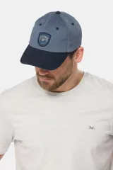 Gorro tipo gorra con visera de lona color azul, con parche tejido frontal que presenta diseño de paisaje y mar.