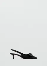 Zapato de tacón tipo slingback en color negro, con diseño destalonado, puntera fina y un detalle de lazo en la parte delantera. Cuenta con tira ajustable en el talón con hebilla metálica dorada y taco fino de altura baja.