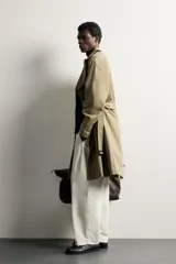 Trench regular fit de color beige, confeccionado en tejido técnico repelente al agua, con diseño de botonadura cruzada, cuello con solapas, mangas raglán con trabillas ajustables en los puños y cinturón del mismo tejido.