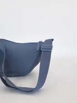 Riñonera de diseño curvo y compacto, con cierre superior y correa regulable que permite llevarla cruzada o al hombro.