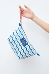 Necessaire de diseño rectangular con estampa de ondas en tonos azules y celestes sobre fondo blanco, con cierre superior y etiqueta frontal con la inscripción Costa Atlántica.