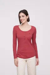 Remera blanca de manga larga, entallada, con cuello redondo y una hilera de botones en el frente. Incluye un pequeño bolsillo decorativo en el pecho.