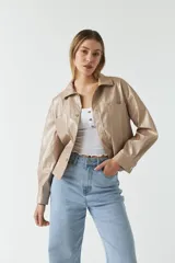 Chaqueta color beige de cuero sintético con cuello clásico, cierre frontal con botones, bolsillos tipo parche en el pecho y corte holgado.