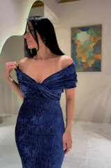 Vestido largo de fiesta en color azul, confeccionado en tela con textura arrugada. Presenta un diseño con escote tipo bardot con nudo central, hombros descubiertos y corte ajustado al cuerpo con una abertura lateral en la falda.