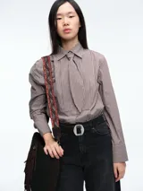 Camisa de manga larga con estampado de rayas verticales en tonos marrones y blancos. Presenta cuello clásico y cierre frontal con botones, acompañada por una corbata del mismo tejido y estampado.