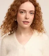 Cardigan cropped de punto color rosa claro, con textura de pelito, cuello en V, mangas largas, cierre frontal con botones y bolsillos delanteros.