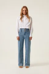 Pantalón de jean celeste de tiro alto, corte recto y pierna ancha. Presenta detalle de trenza en la cintura y pliegue a media pierna.
