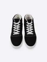 Bota de lona estilo urbano, color negro con costuras blancas visibles, cordones blancos y suela de goma blanca.