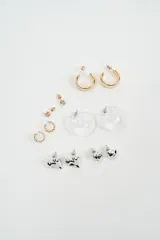 Set de aros variados que incluye aros tipo argolla dorados, aros con piedra brillante, aros tipo argolla de acrílico transparente, aros con diseño de hojas y aros con forma de corazón plateado.