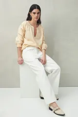 Blusa blanca de algodón con escote en V y mangas 3/4 bordadas con motivos florales y aberturas lineales. Puños con elástico.