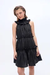 Vestido corto negro sin mangas, con cuello alto fruncido tipo gorguera y volados en los hombros. Presenta diseño en niveles con fruncidos horizontales.